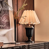 Urn base lamp lit on a carved cabinet beside a framed print
