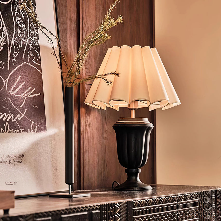 Urn base lamp lit on a carved cabinet beside a framed print