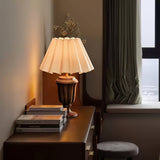 Urn base lamp lit on a dark desk beside stacked books and a stool