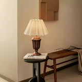 Urn base lamp lit on a small round table beside a wood bench