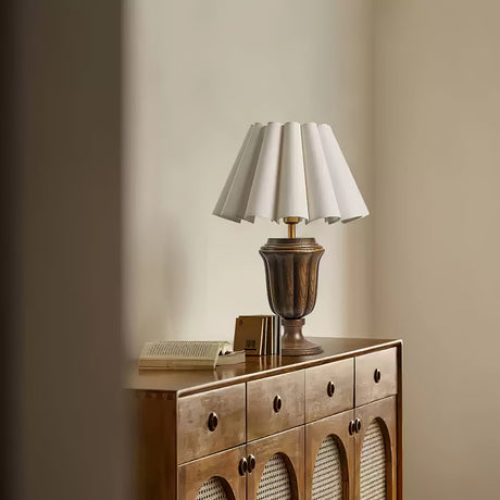 Urn base lamp lit on a cane fronted sideboard against a pale wall