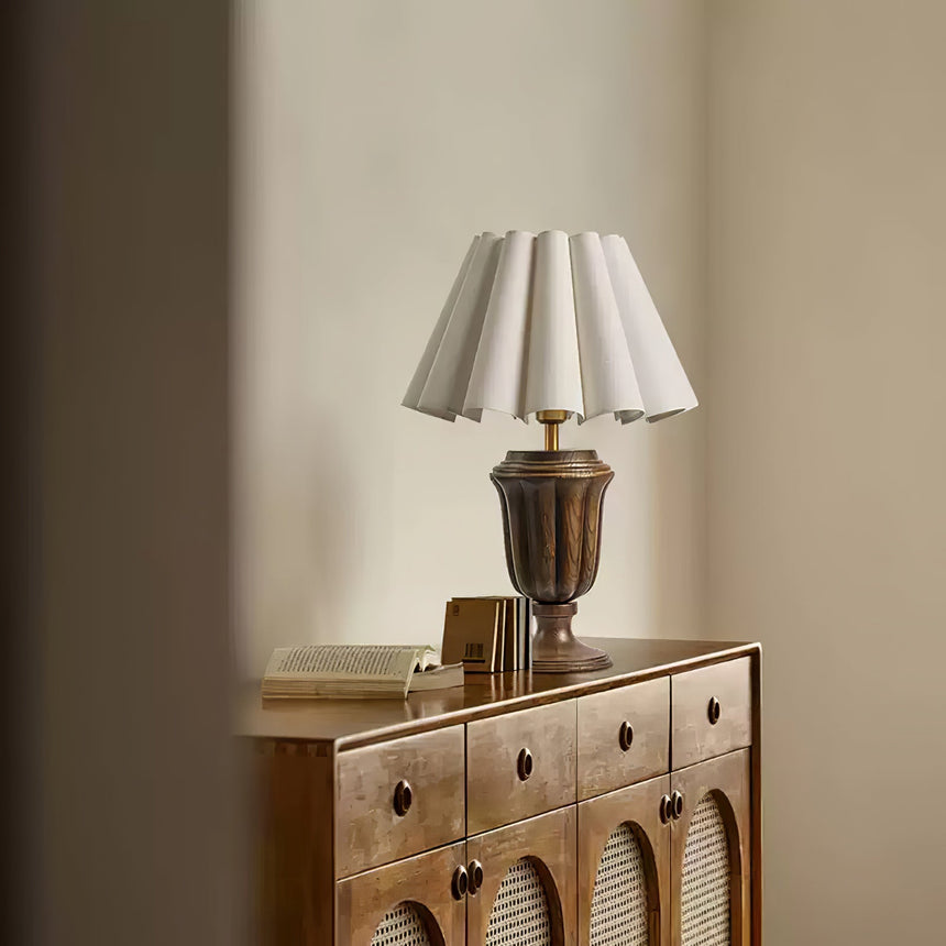 Urn base lamp lit on a cane fronted sideboard against a pale wall