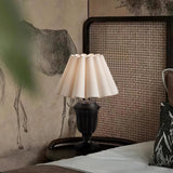 Urn base lamp lit beside a cane headboard and a green plant
