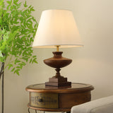 Walnut oversized table lamp lit on a round table beside a green plant