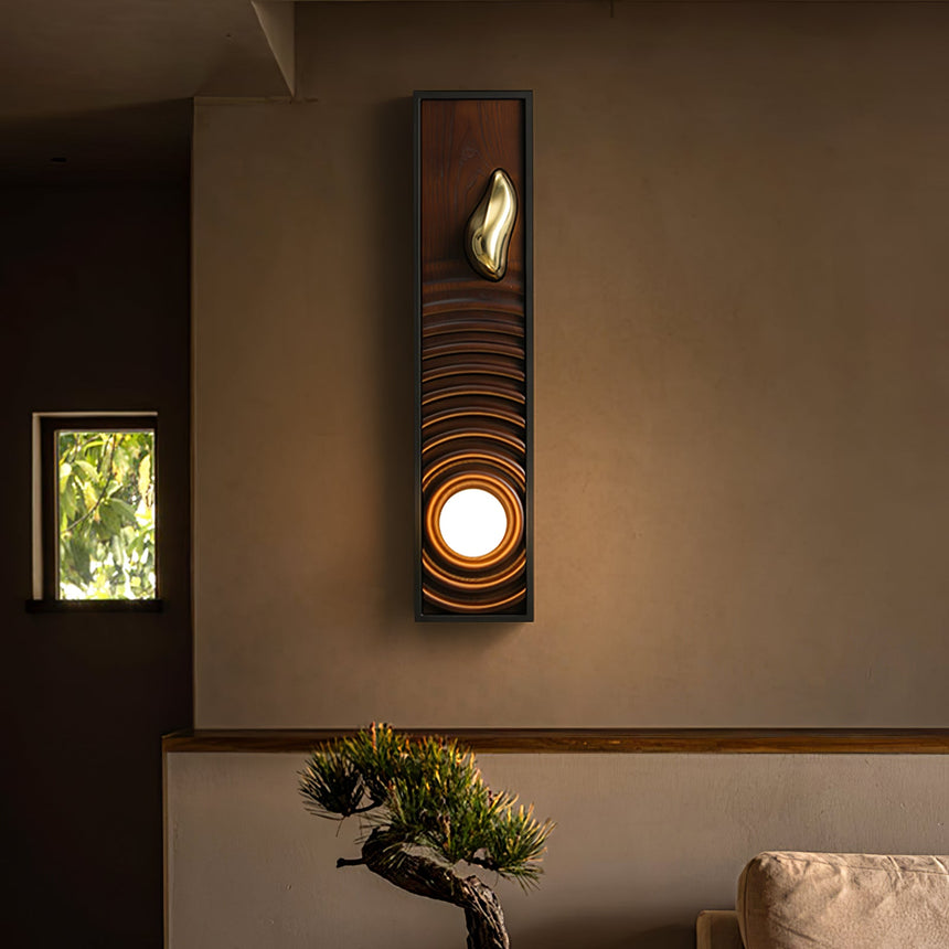 Sconce lit on a plaster wall beside a small window with a bonsai on a low table