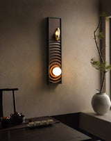 Sconce lit above a long wood console holding a vase of branches and a tray