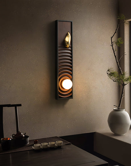Sconce lit above a long wood console holding a vase of branches and a tray