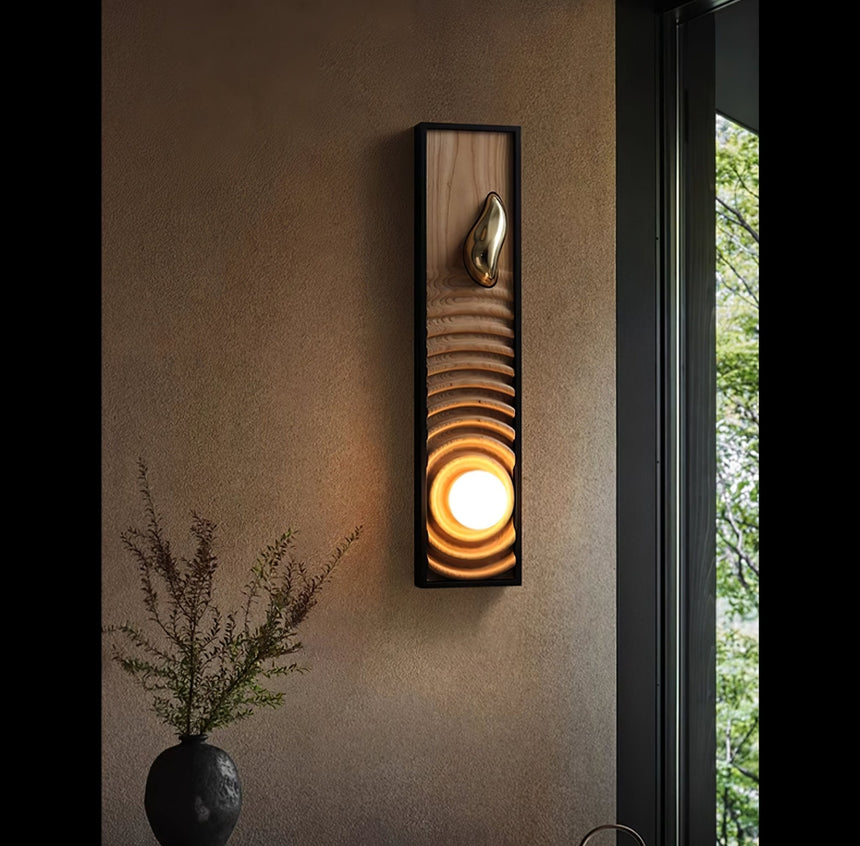 Sconce lit on a wall beside a window with a vase of green branches below