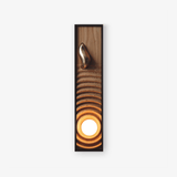 Oversized wall sconce, a tall black frame holding a rippled wood panel and a lit orb