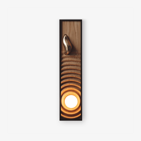 Oversized wall sconce, a tall black frame holding a rippled wood panel and a lit orb