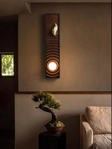 Sconce lit above a bonsai on a stand beside a pale armchair and a window