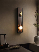 Sconce lit above a dark sideboard with a teapot, a tray and a tall vase
