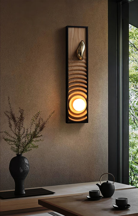 Sconce lit above a low tea table set with cups beside a tall window
