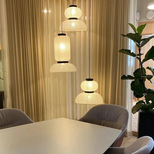 Rice paper lanterns lit above a dining table in front of tall curtains
