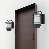 Two lanterns on a white wall on either side of a tall dark brown door