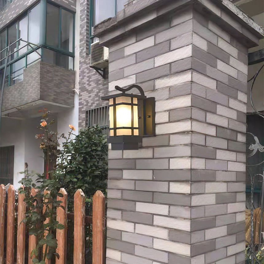 The lantern on a gray brick gate pillar above a wood picket fence