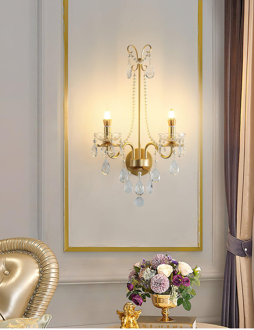 The pearl sconce lit inside a gold framed panel above a table with flowers