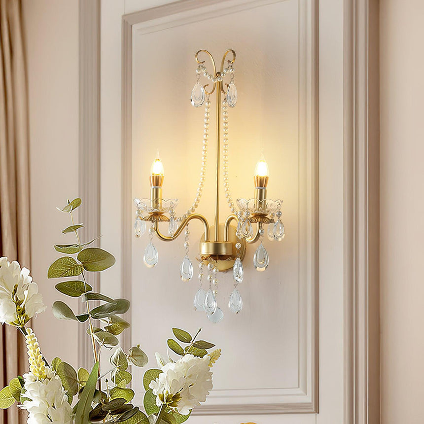 The pearl sconce lit on a paneled wall above a vase of white flowers