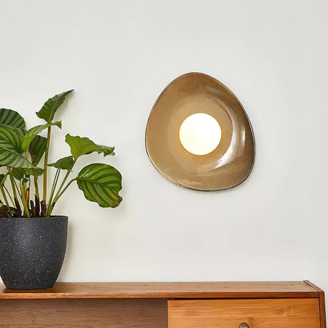 The pebble light lit above a teak sideboard, the glaze warming around the globe