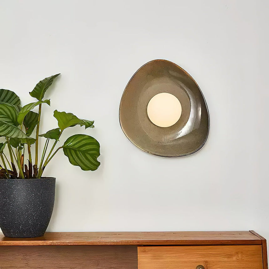 The pebble light above a teak sideboard beside a potted plant with striped leaves
