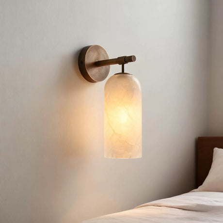 The sconce glowing warm on a pale wall above a bed headboard
