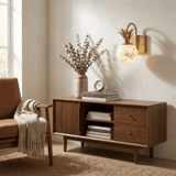 The sconce lit above a walnut console with a vase of dried stems