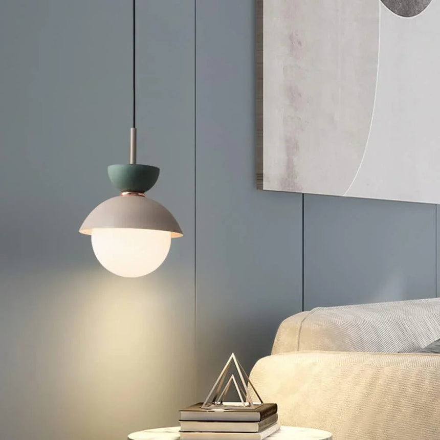 A capped opal globe lit on a pale wall beside a tall cactus