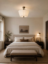 Pleated fabric ceiling light lit in a bedroom with a framed landscape and a lamp