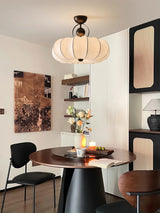 Pleated silk ceiling light above a dining table with black chairs and framed art