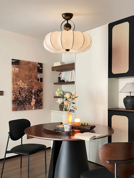 Pleated silk ceiling light above a dining table with black chairs and framed art