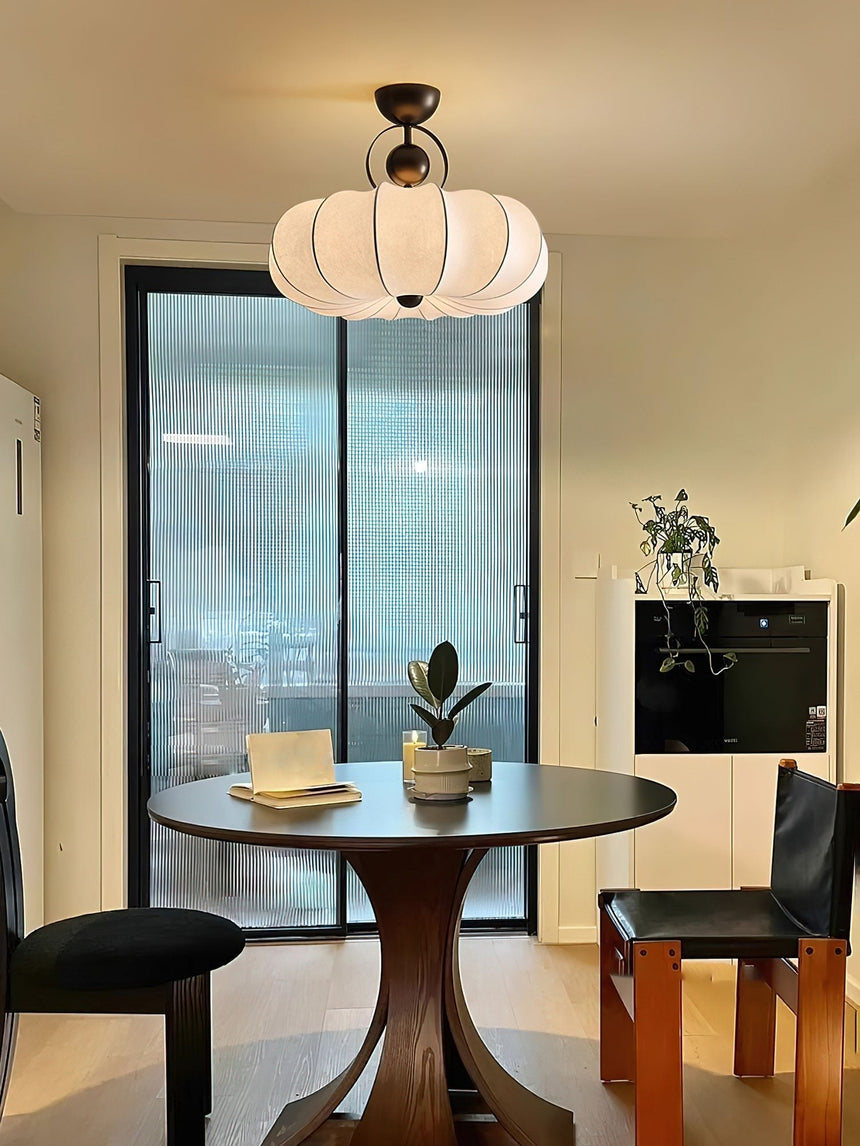 Pleated silk ceiling light lit above a pedestal table near a tall window