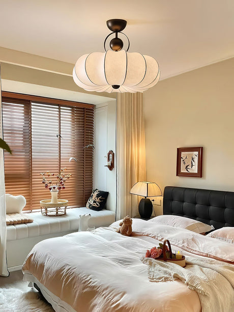 Pleated silk ceiling light lit in a bedroom with wood blinds and a dark headboard