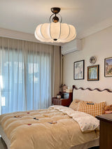 Pleated silk ceiling light above a bed with framed pictures and a sheer curtain