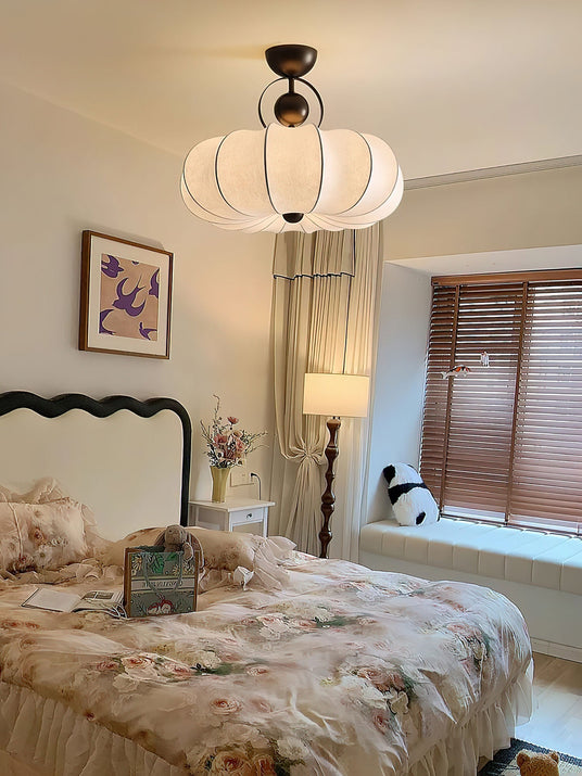 Pleated silk ceiling light in a bedroom with a carved headboard and a table lamp