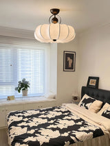 Pleated silk ceiling light lit over a bed with black and white bedding
