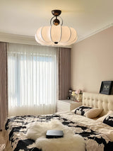 Pleated silk ceiling light above a bed with a tufted headboard and long curtains