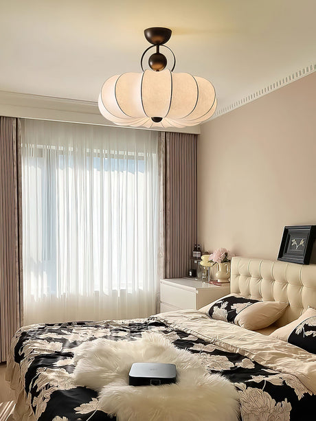 Pleated silk ceiling light above a bed with a tufted headboard and long curtains