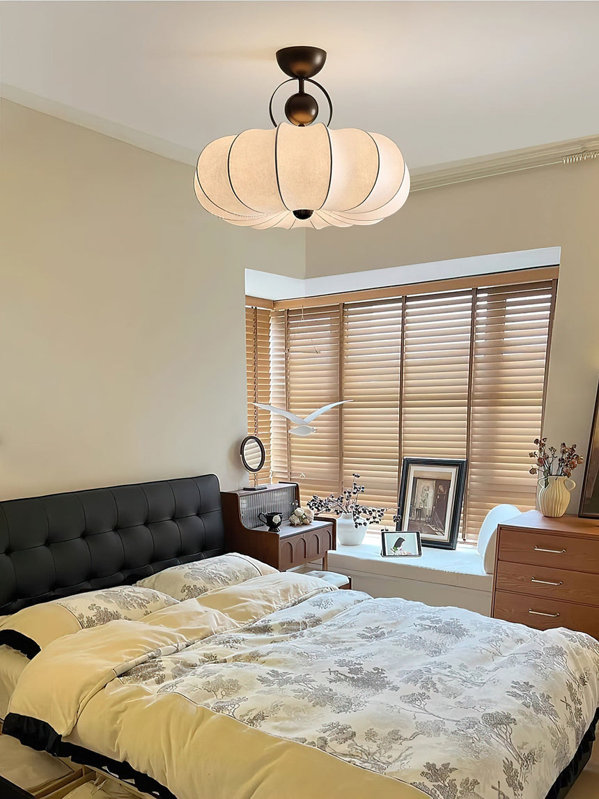 Pleated silk ceiling light lit above a bed with yellow bedding and a round mirror