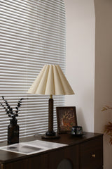 Pleated table lamp unlit beside a window with dried branches