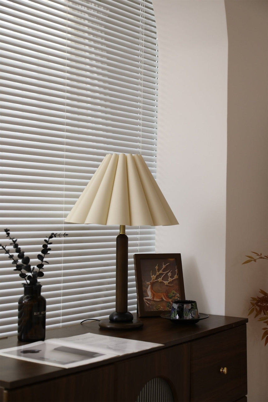 Pleated table lamp unlit beside a window with dried branches