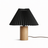 Pleated black shade on a pale wood cylinder base against a white ground