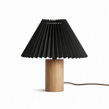 Pleated black shade on a pale wood cylinder base against a white ground