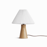 Pleated white shade on a short pale wood base seen against a white ground