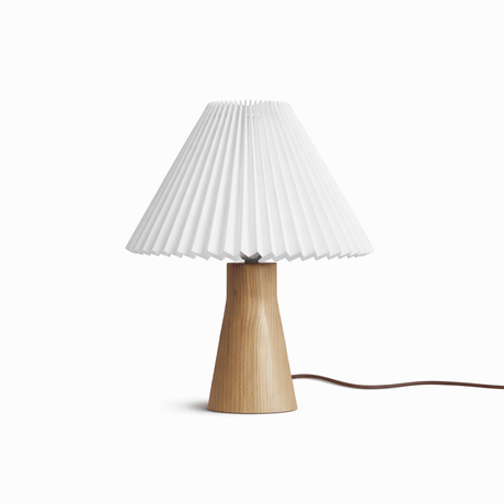 Pleated white shade on a short pale wood base seen against a white ground