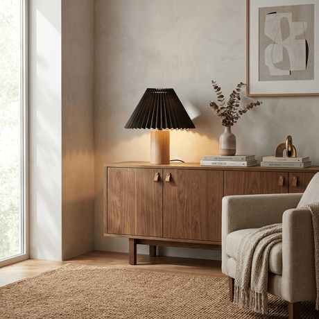 Pleated table lamp lit on a wood sideboard beside books and a vase
