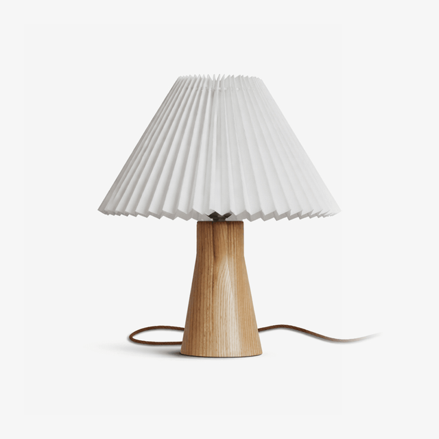 Pleated table lamp with a white shade on a pale wood base, plain ground