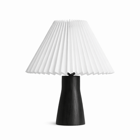 Tall black base under a pleated white shade against a plain white ground