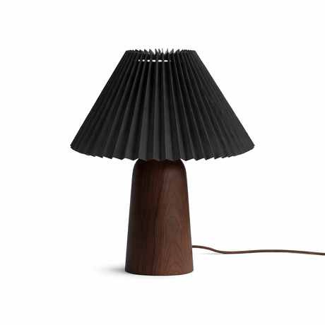 Pleated black shade on a walnut base seen front on against a white ground
