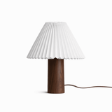 Pleated white shade on a walnut base seen front on against a white ground