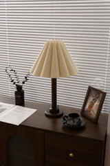 Pleated table lamp seen across a room on a dark wood dresser